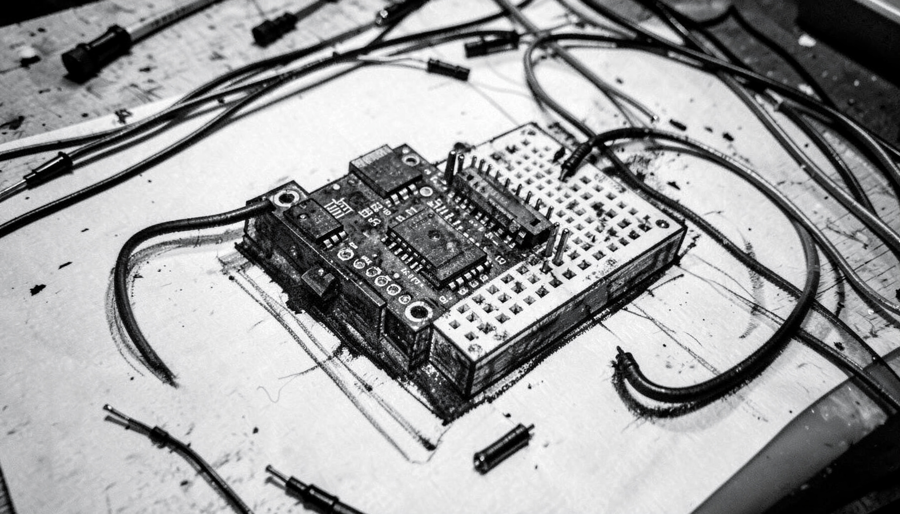 A bold charcoal drawing of an Arduino Uno board with wires connecting to a small breadboard, loose jumper cables curling across a workbench surface in moody monochrome.